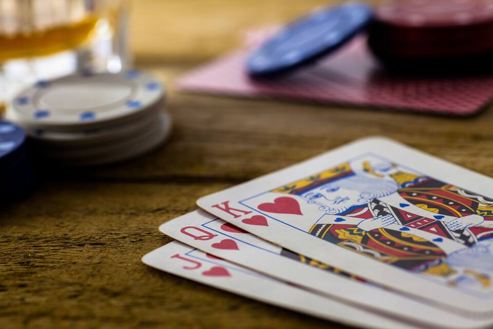 Ett träbord med spelkort, pokermarker och ett glas med en bärnstensfärgad vätska.