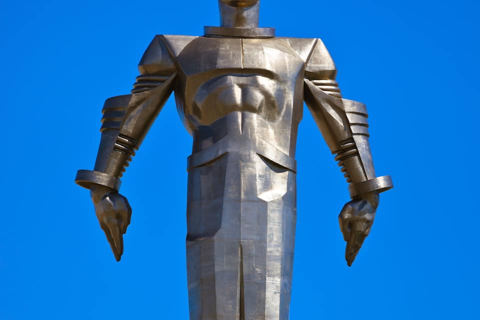 A tall, metallic statue with a human figure, set against a clear blue sky.