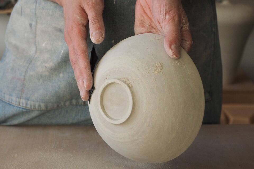 A person in a denim apron holding a clay pot.