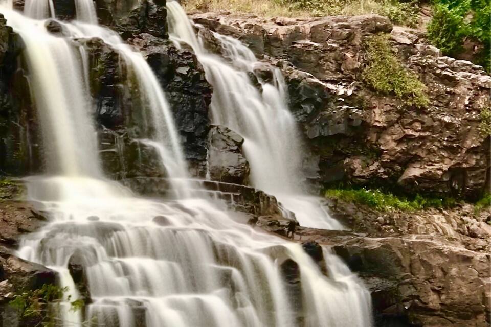 Une cascade à plusieurs niveaux dévalant un terrain rocheux, entourée d’une végétation luxuriante.