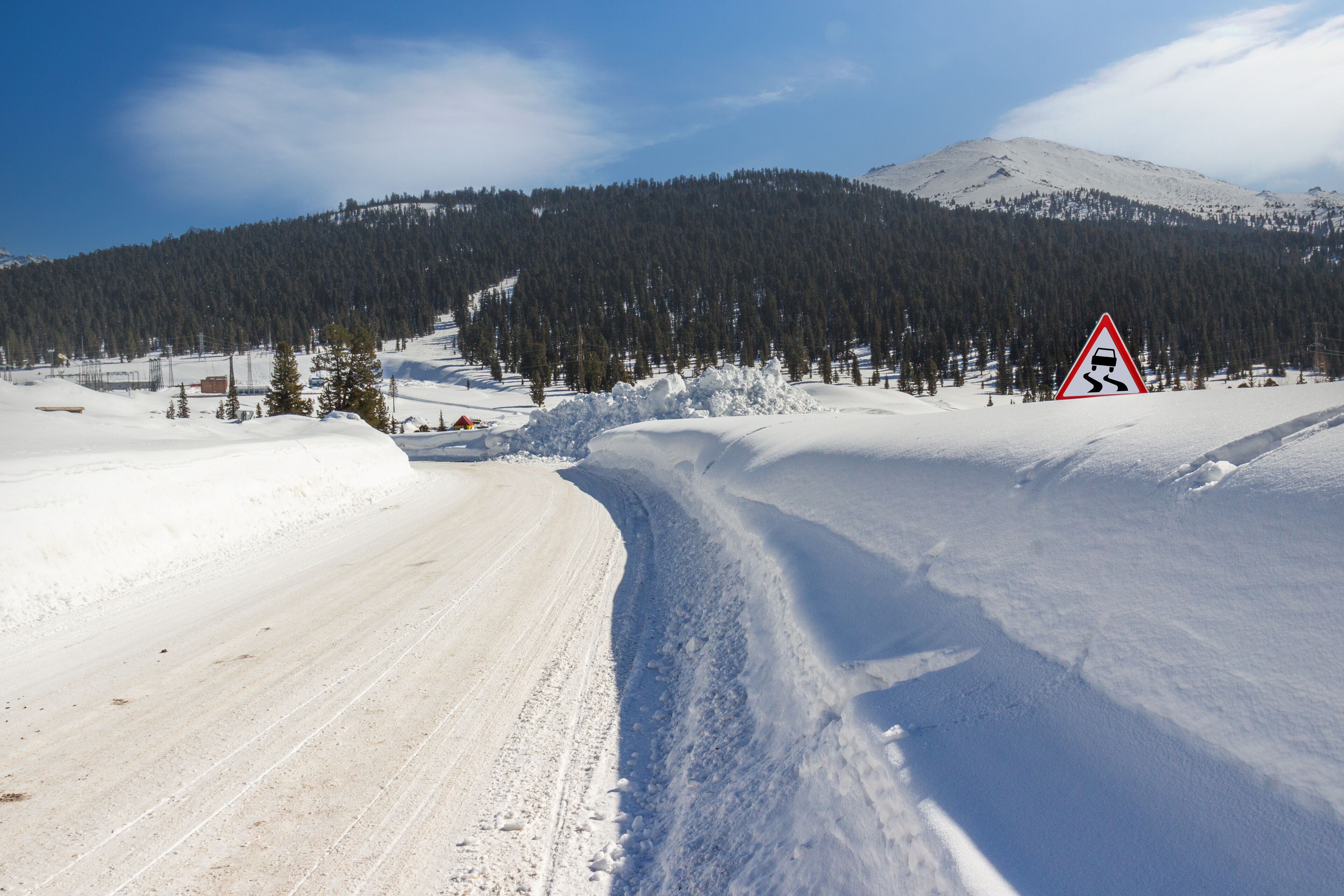 Mountain road on a sunny day. Winter driving on curvy snowy highway. Road signs on the side of the road are covered with deep snowdrifts. Western Sayan mountains, Siberia, Russia.