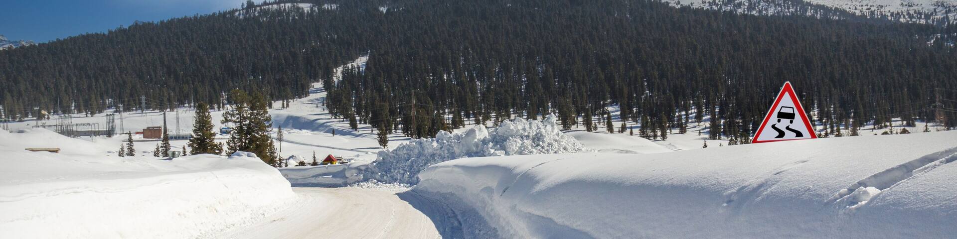Mountain road on a sunny day. Winter driving on curvy snowy highway. Road signs on the side of the road are covered with deep snowdrifts. Western Sayan mountains, Siberia, Russia.