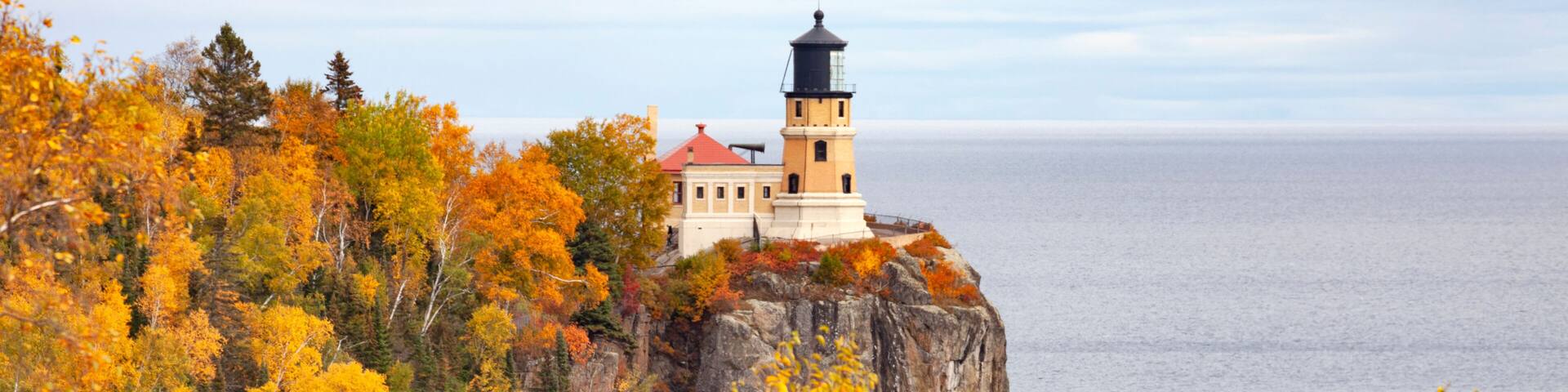 A lighthouse on a cliff surrounded by autumn foliage.