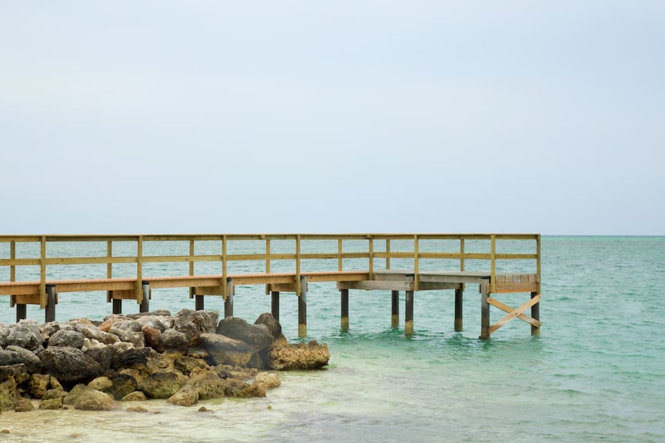 A wooden pier extending into calm turquoise waters, supported by rocks and wooden posts.