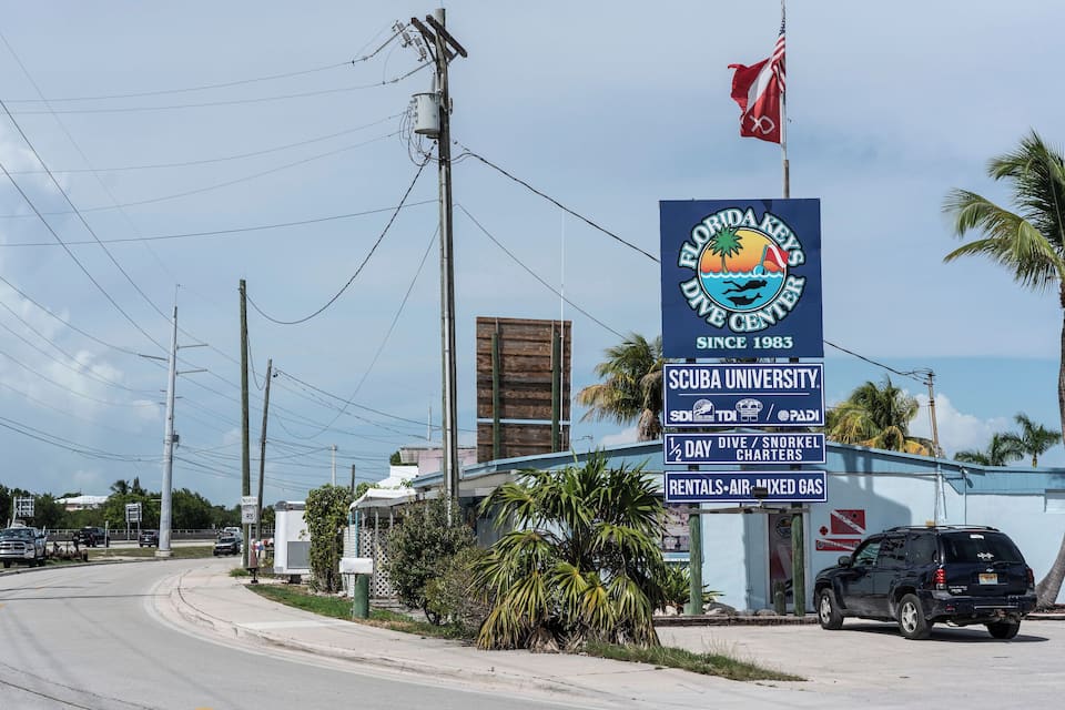 A sign for the Florida Keys Dive Center with a palm tree and a black SUV parked nearby.