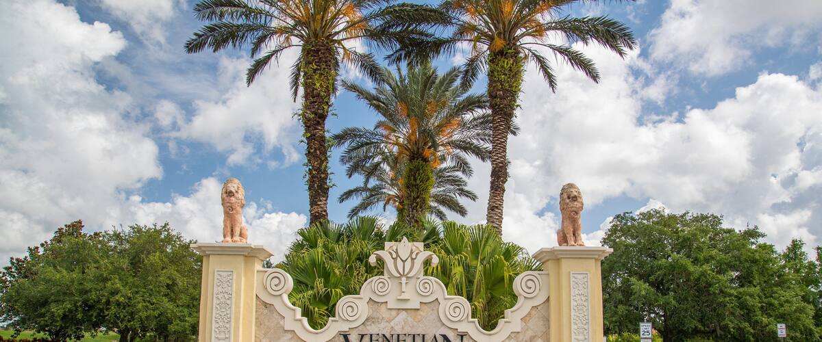 A sign for Venetian Golf & River Club with a fountain and palm trees in the background.