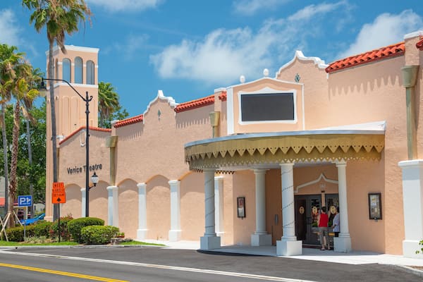 A building with a theater entrance, palm trees, and a clear sky.