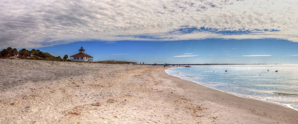 A sandy beach with a lighthouse and palm trees.