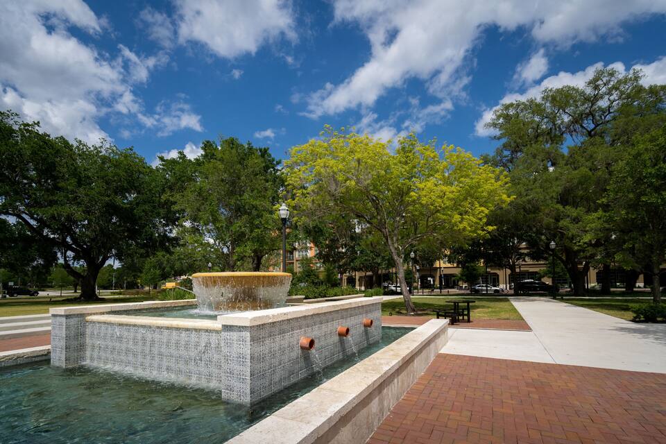 A fountain with water spouting from three pipes, surrounded by a tiled pool and trees.