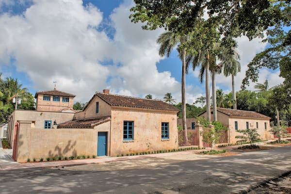 A two-story building with a tiled roof, surrounded by palm trees and a clear sky.