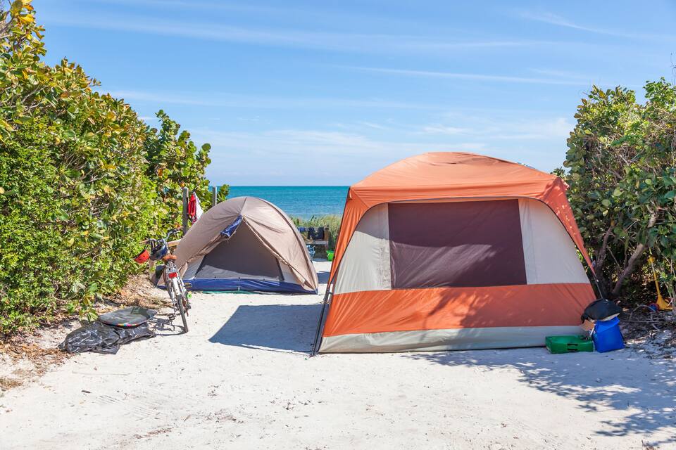 Duas tendas numa praia arenosa, com céu azul límpido e vegetação verde.