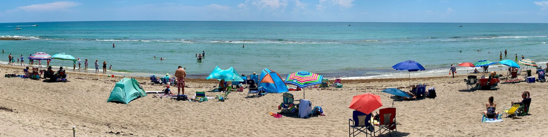 Una playa con gente tomando el sol, sombrillas y tiendas de campaña.