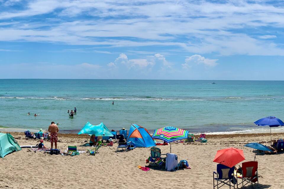 A beach with people sunbathing, umbrellas, and tents.
