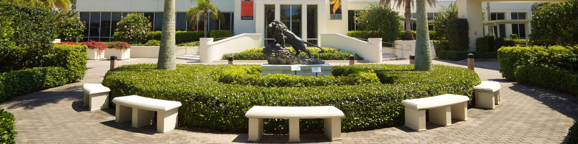 The Vero Beach Museum of Art with a central sculpture, palm trees, and a paved walkway.