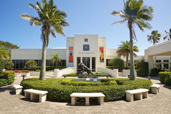 The Vero Beach Museum of Art with a central sculpture, palm trees, and a paved walkway.