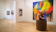 An art gallery with wooden floors and various paintings and sculptures.