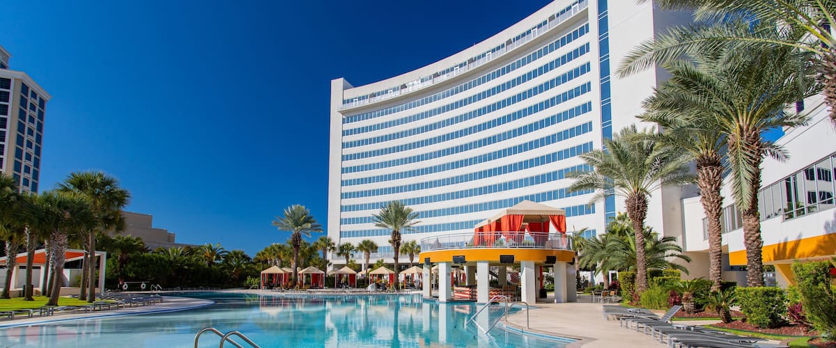 A swimming pool with lounge chairs and palm trees, surrounded by a modern building with a curved facade.