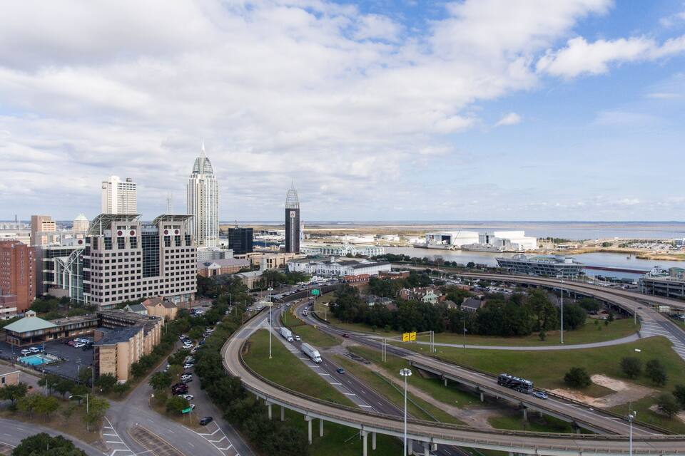 Un paisaje urbano con un rascacielos destacado, un río y un cruce de autopista.
