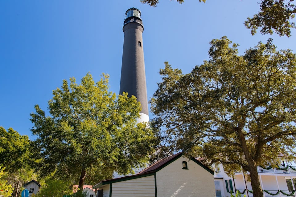 Um farol cercado por árvores e um edifício branco com detalhes verdes.