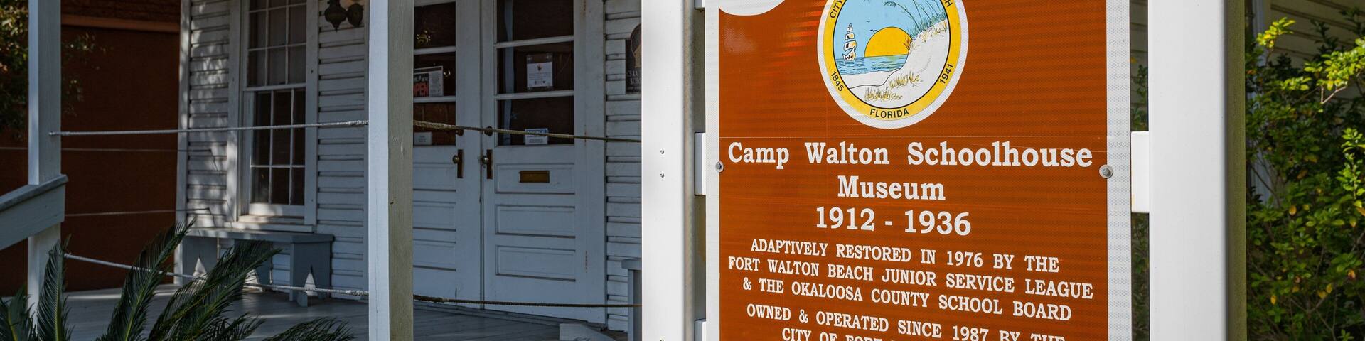 Una escuela de madera con un cartel que detalla su historia como el Museo Escuela Camp Walton, operativa desde 1912 hasta 1936.