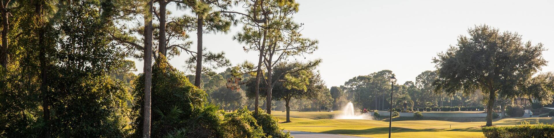 A golf course with a pond, trees, and a fountain.