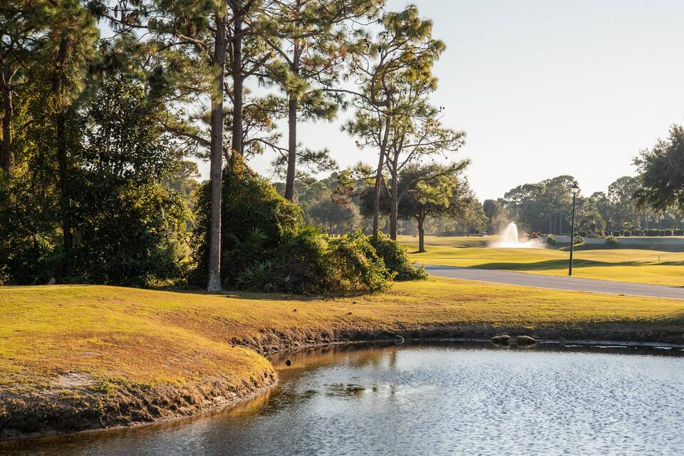 Ein Golfplatz mit Teich, Bäumen und einer Fontäne.
