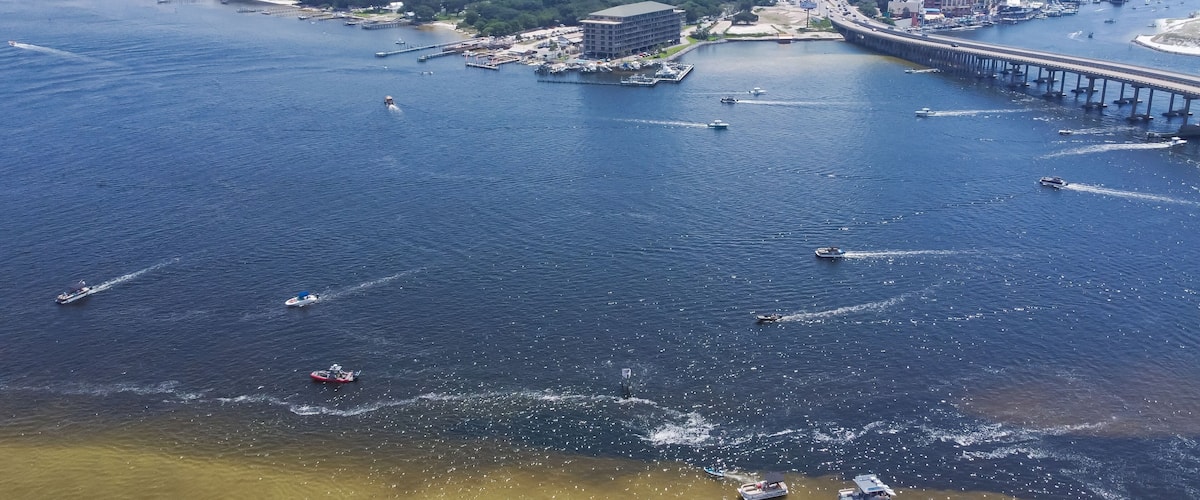 Downtown Destin Florida with Destin Bridge or William T. Marler Bridge connect Santa Rosa Island beach near Crab Island with busy speeding boats on turquoise water along Gulf of Mexico