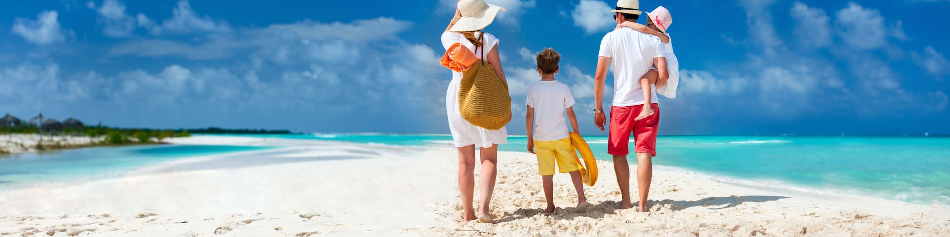 A family on a white sandy beach with clear turquoise water and a blue sky.