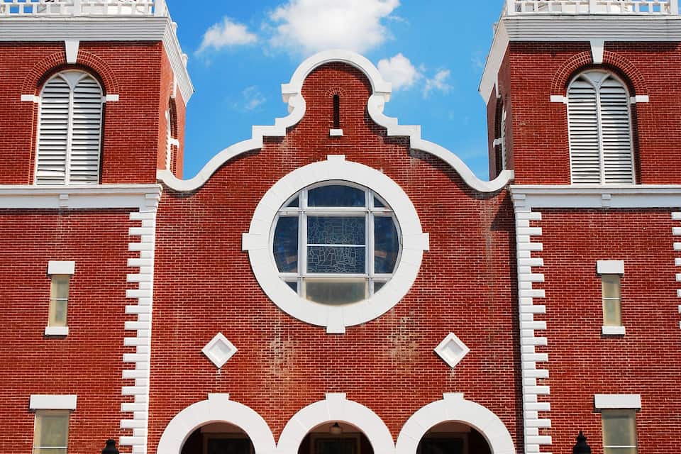 Um edifício de tijolos vermelhos com duas torres, uma grande janela circular e um conjunto de escadas que levam à entrada.