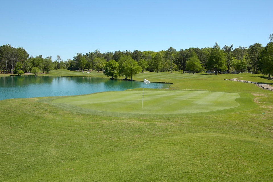 A golf course with a pond, green hills, and trees.