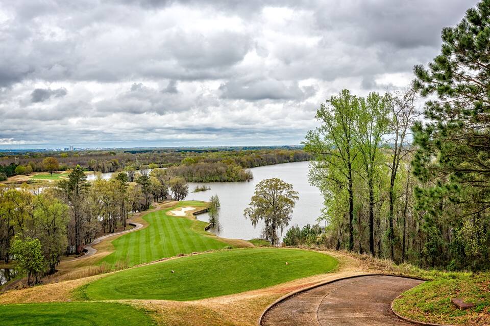 Um campo de golfe com um lago, rodeado por árvores e um céu nublado.