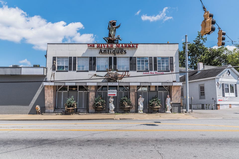 A building with a sign reading "The River Market Antiques" and a statue of a man on top.