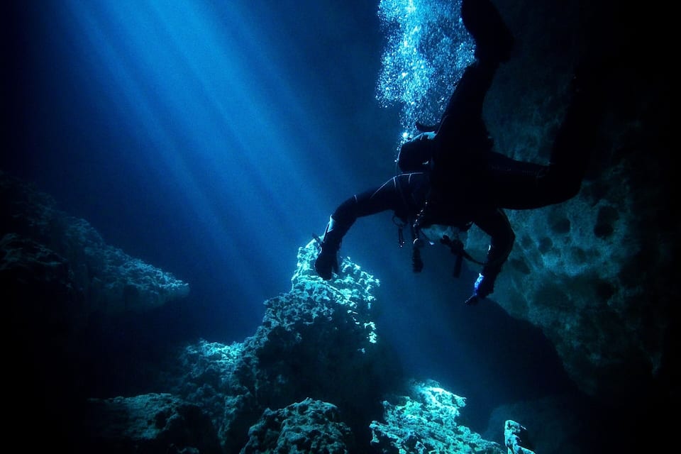 A diver exploring an underwater cave with blue lighting.
