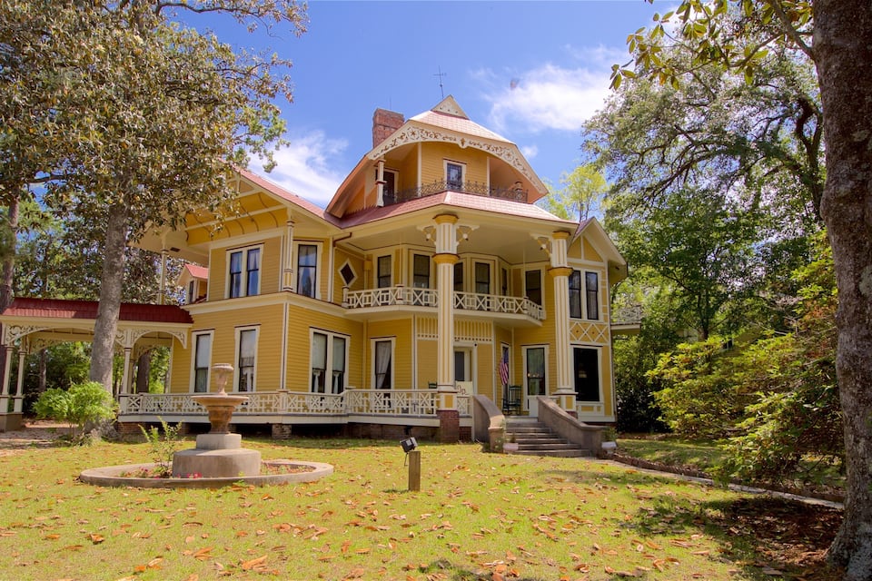 Una grande casa gialla a più piani con un portico che circonda l'edificio e una fontana nel giardino.