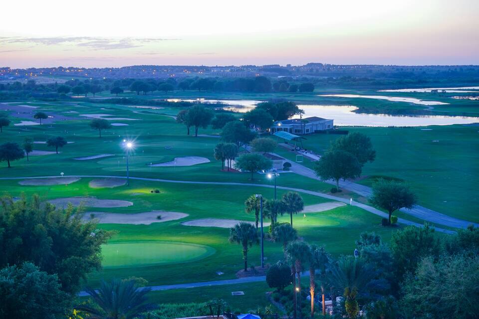 A golf course at dusk with water bodies and trees.