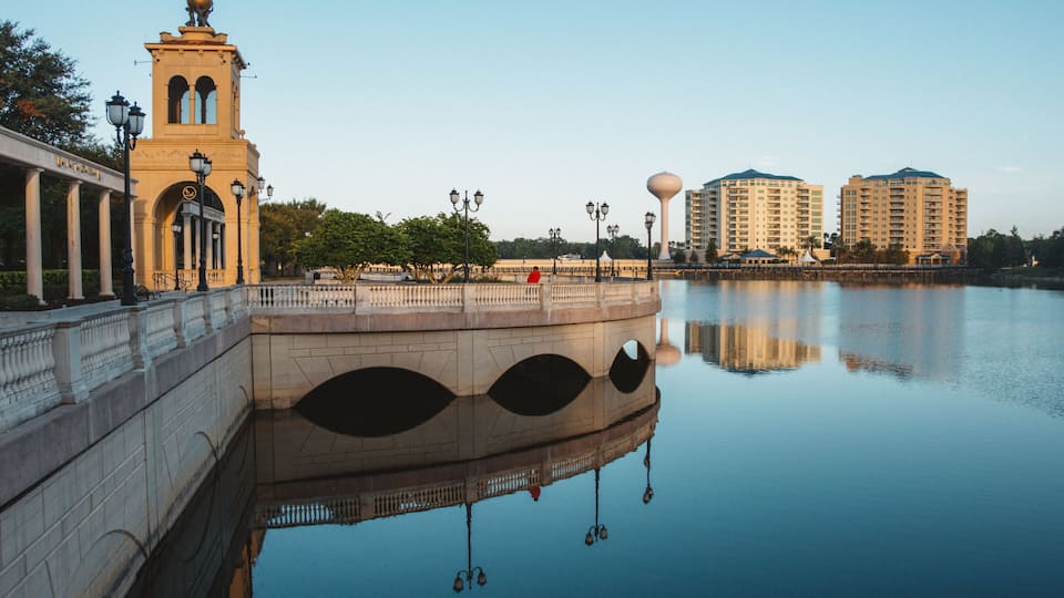 A bridge with a tower, a calm river, and modern buildings in the background.