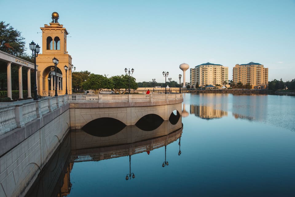 Uma ponte com uma torre, um rio calmo e edifícios modernos ao fundo.
