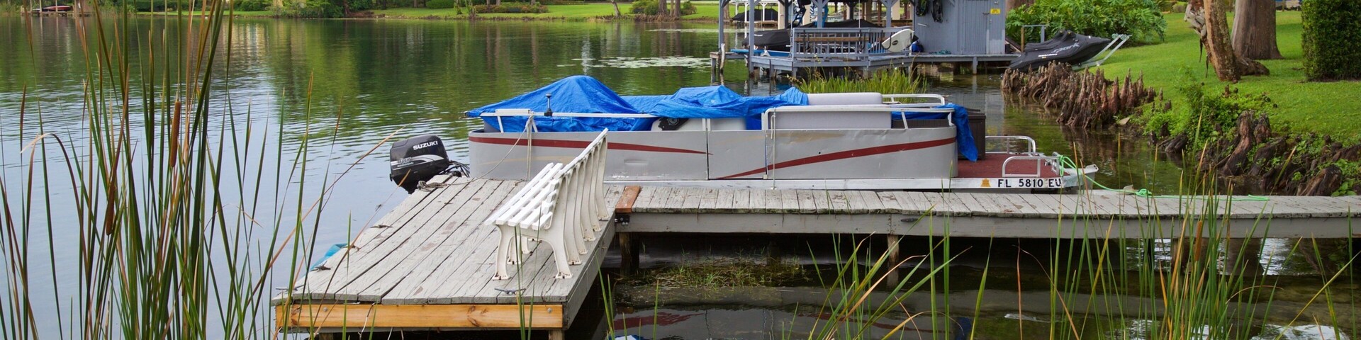 Um cais com um barco, uma estrutura coberta e uma casa em um cenário à beira de um lago.