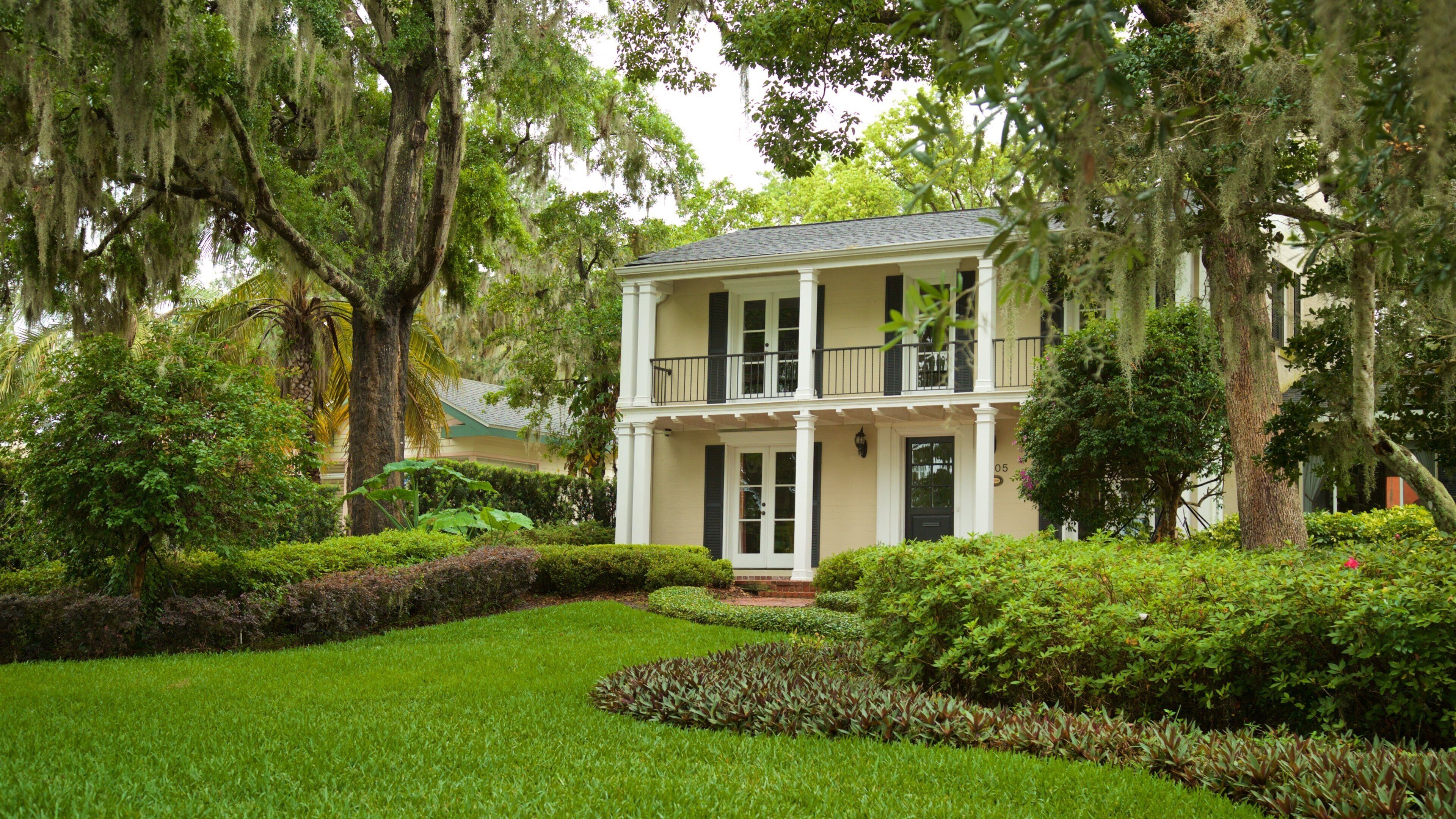 A two-story house with a balcony, surrounded by lush greenery and trees.