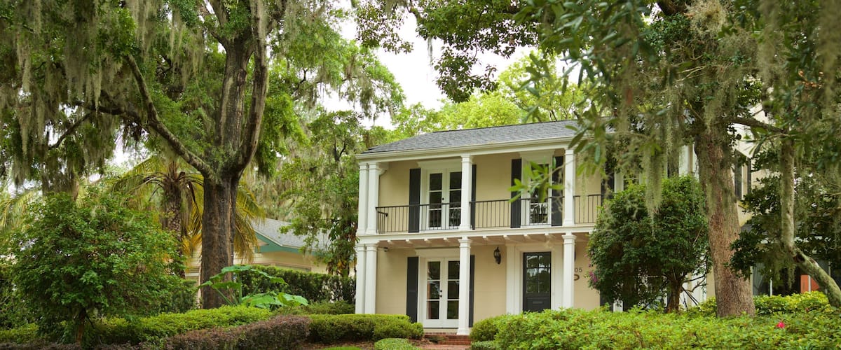 A two-story house with a balcony, surrounded by lush greenery and trees.