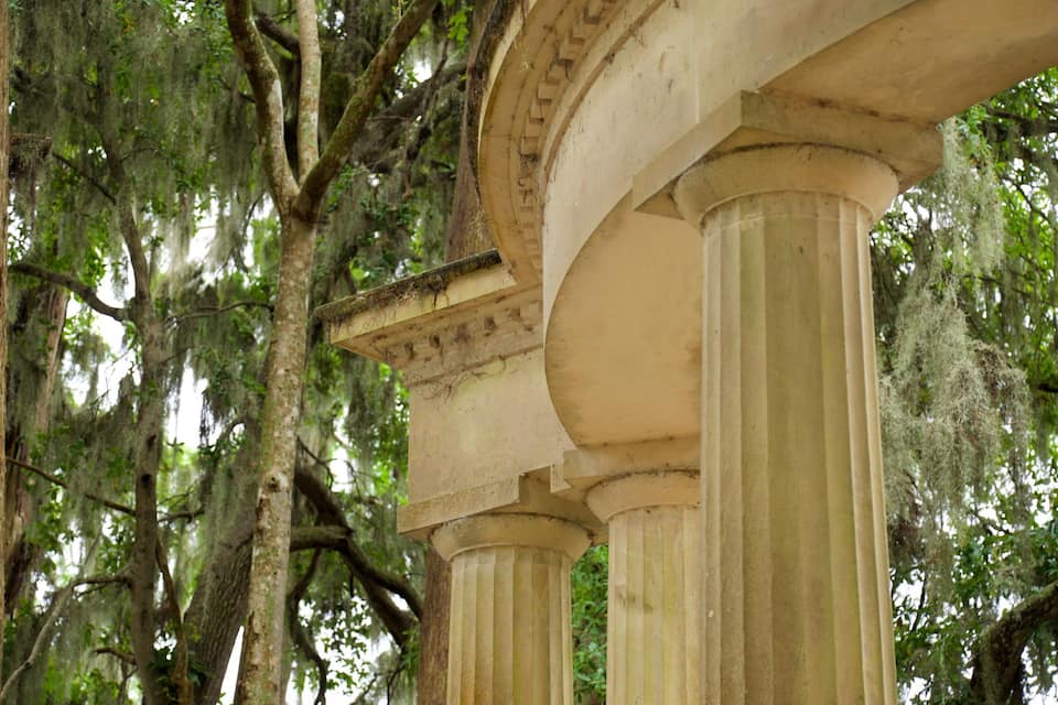 Un edificio storico con grandi colonne e alberi ricoperti di muschio.