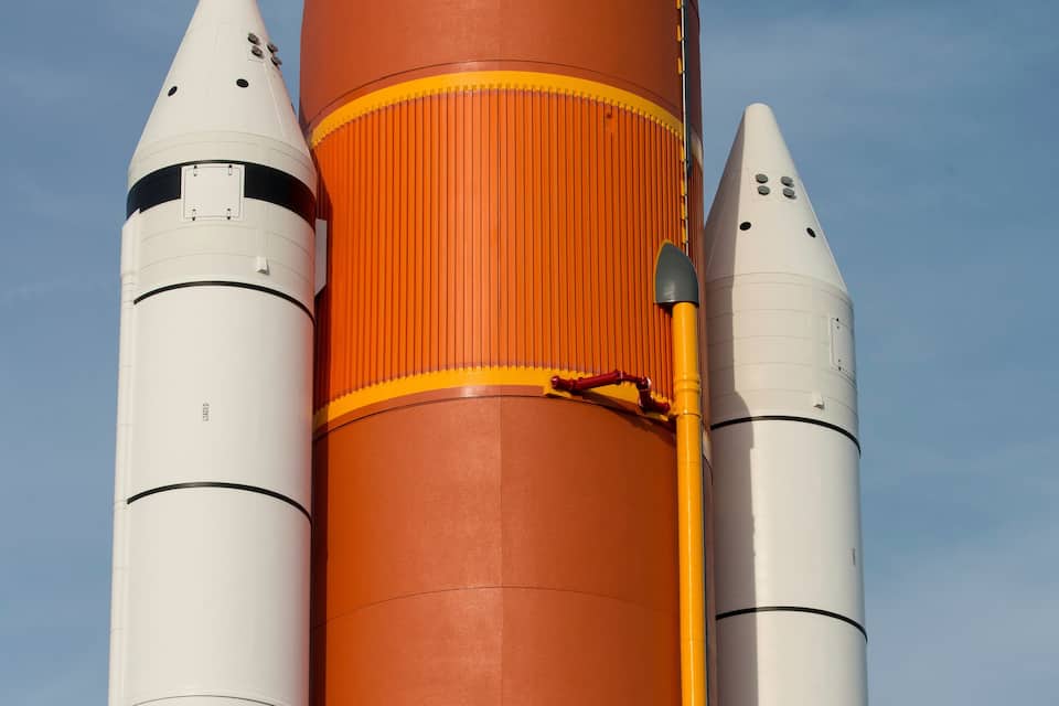 A rocket with an orange and white body, a bird perched on a structure, and a clear blue sky in the background.