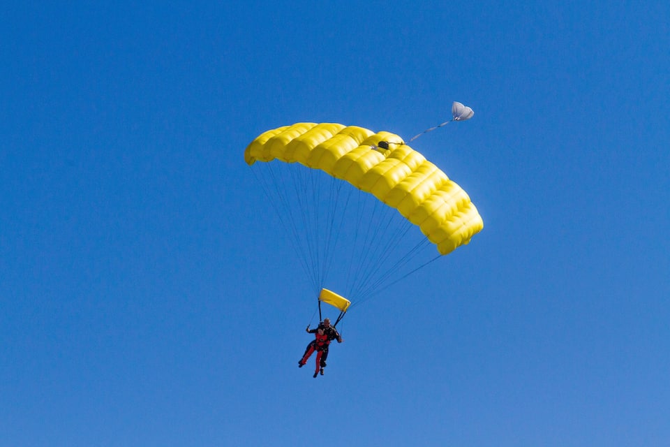 A person skydiving with a yellow parachute against a clear blue sky.