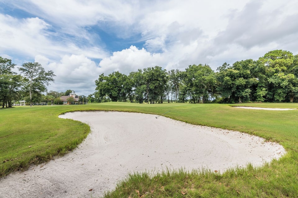 A golf course with a sand bunker, green grass, and trees.