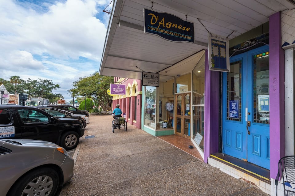 A street with a blue door art gallery, a clothing store, and a sign for a real estate agency.