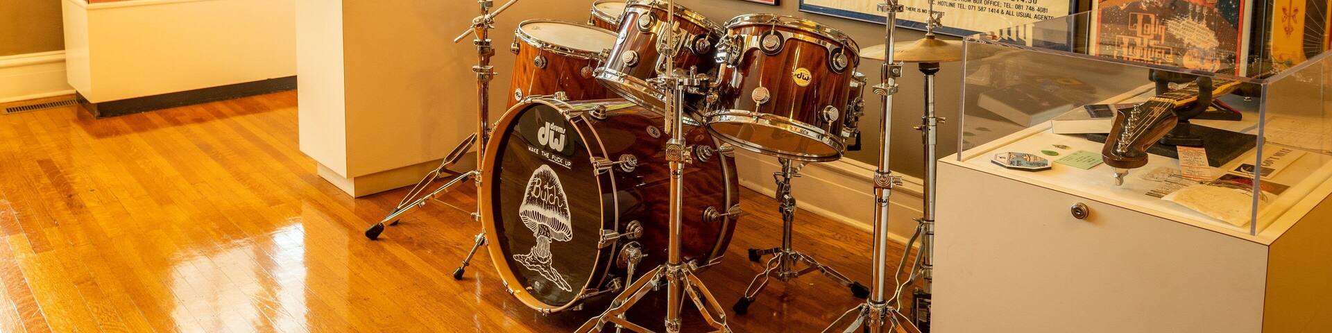 A drum set in a room with wooden floors and walls adorned with framed posters.