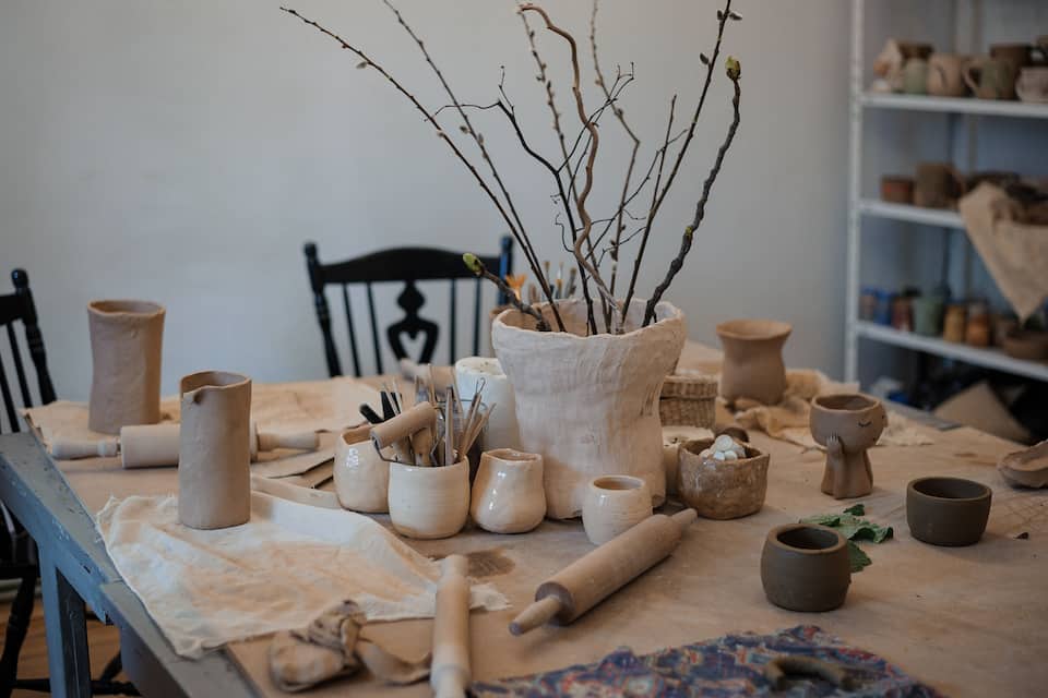 Pottery items, including pots and a branch, on a table with a rolling pin and cloth.