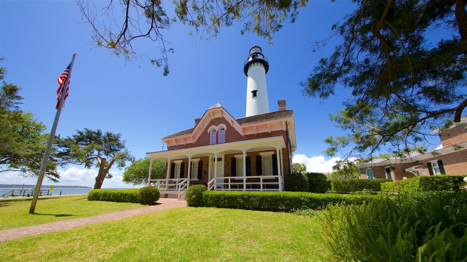 A lighthouse with a white tower and a brick building with a porch in front.