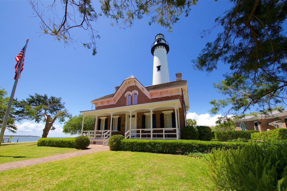 A lighthouse with a white tower and a brick building with a porch in front.