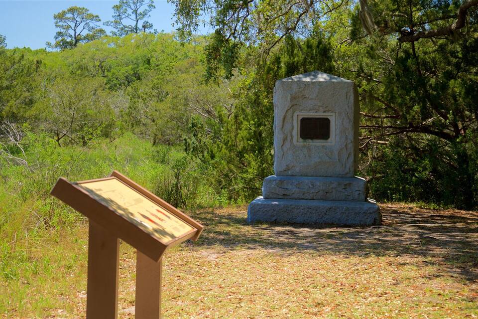 A stone monument with an inscription plaque in a grassy area surrounded by trees.